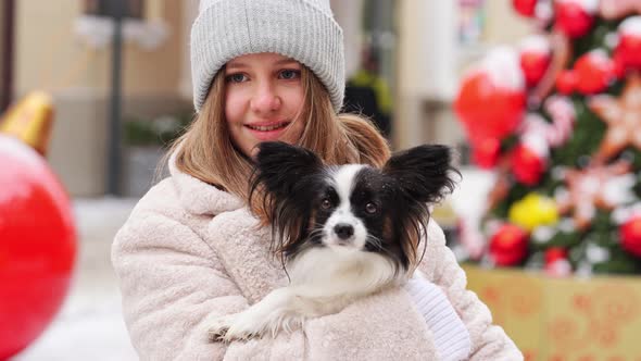 Beautiful Girl with Dog Papillon in Her Arms on Winter Christmas Streets alt
