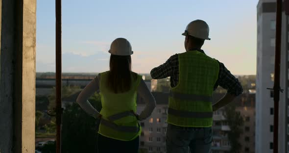 Builders Look at a Cityscape on a Sunset Background Back View alt