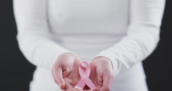 Mid section of woman holding a pink ribbon against black background alt