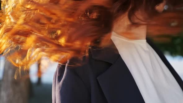 Woman in Jacket Shakes Copper Hair Standing on City Street alt