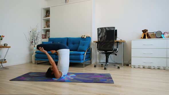 Young Woman Does Yoga At Home Bending Knees To Her Chest In Pindasana Pose