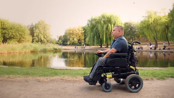 Wheelchair Man. Handicapped Man. a Young Disabled Man in an Automated Wheelchair Walks By the Lake alt