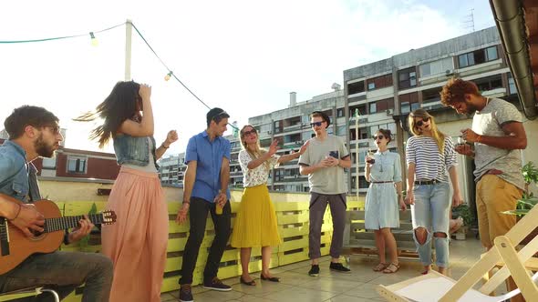 Happy people dancing and playing guitar at the rooftop party on sunny day alt
