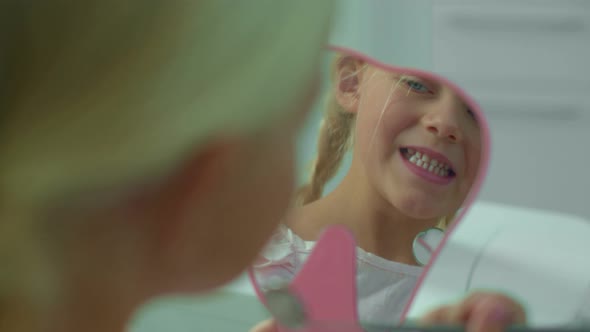 Small Girl Smiles in the Mirror and Clicks Her Jawbone. alt