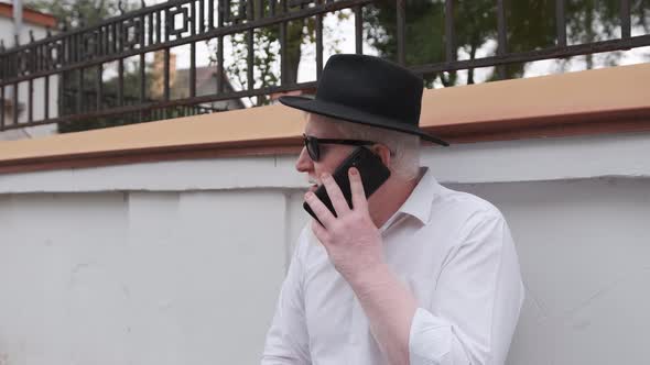 Old Man with Albinism Talking on the Phone While Sitting Next To His House alt
