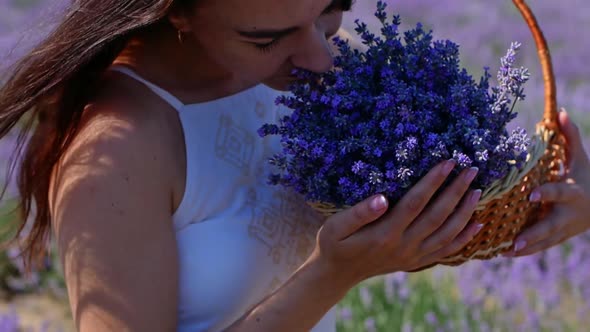 A young woman in a hat and white dress holds a wicker basket with lavender flowers. alt