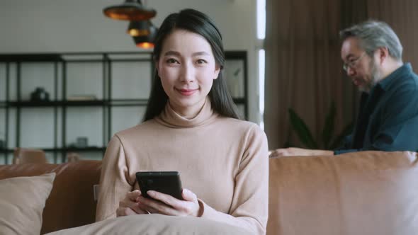 asian attractive female wife hand hold smartphone on sofa at living room