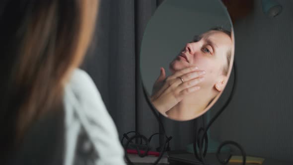 Young Woman Looks at Herself in the Mirror Examines the Skin of Her Face and Gets Upset