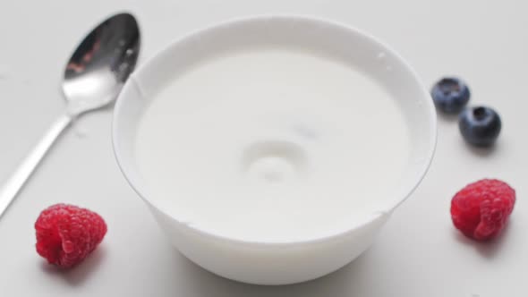 Raspberries and blueberry falling into white bowl with yogurt and whipped cream.