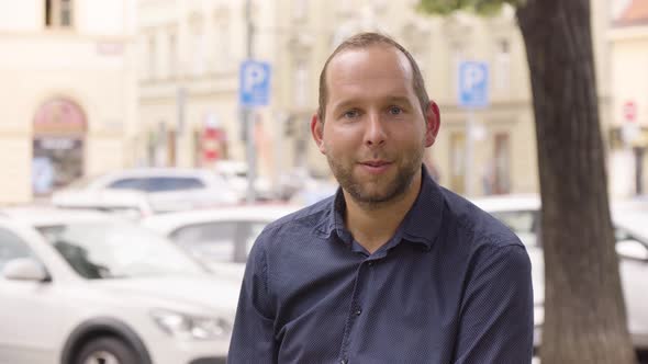 A Caucasian Man Talks to the Camera with a Smile in an Urban Area  a Colorful Street