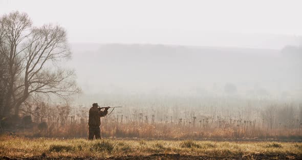 Hunter in hunting equipment look at the target and aim with shot gun in the field foggy morning  alt
