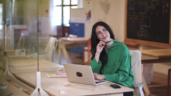 Businesswomanusing laptop in office, laughing, holding eyeglasses