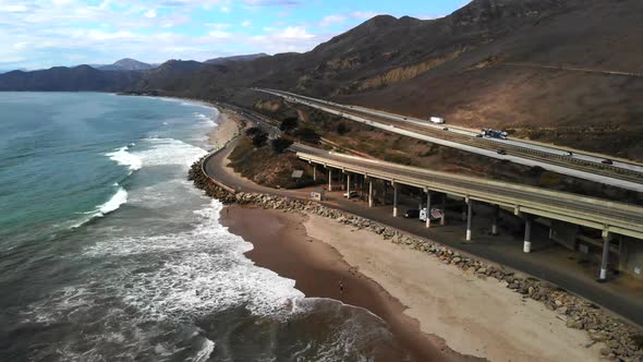 Aerial drone shot over a concrete bridge on the beach in Ventura next to the blue ocean waves and ca alt