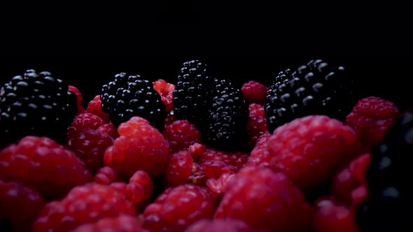 Blackberries and raspberries on a black background, close up view