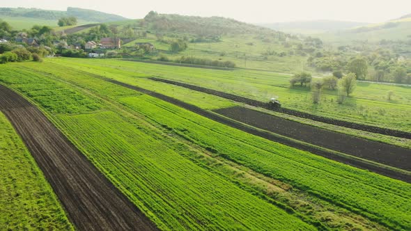 Drone Flight Over Green Spring Crops Growing in Agricultural Fields with a Tractor alt