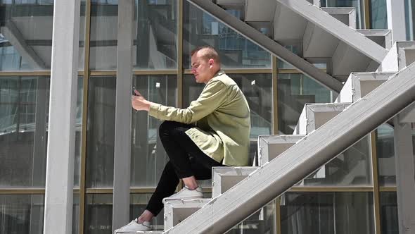 Young Man Sitting on the Stairs and Talking Sign Language Via Video Link on Smartphone Outdoors alt