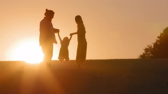 Family Silhouettes Parents with Child Plays Dad and Mom on Field in Sunset Light Flying in Air alt