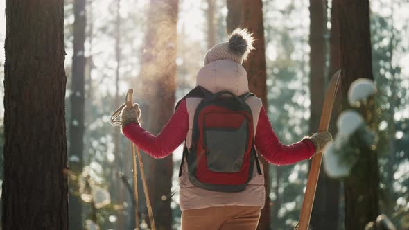 Woman with Skis and Backpack Looks Around in Winter Forest alt