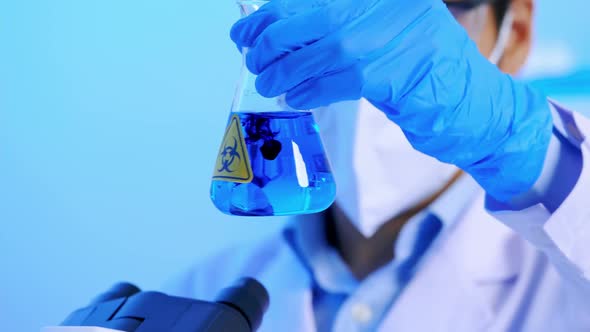 Asian scientist doing some research checking a liquid in a test flask at laboratory. alt