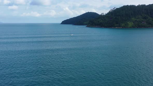 AERIAL: drone flying through the atlantic ocean with a view of a small sailing boat near an island alt