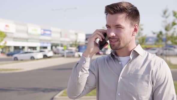 A Young Caucasian Man Talks on a Smartphone in an Urban Area alt