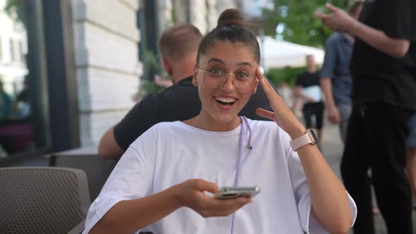 Beautiful Young Woman Sitting in Street Cafe Using a Smartphone alt