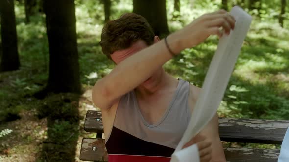 A Guy Sits on a Bench in the Woods and Pulls Out a Long Receipt Tape