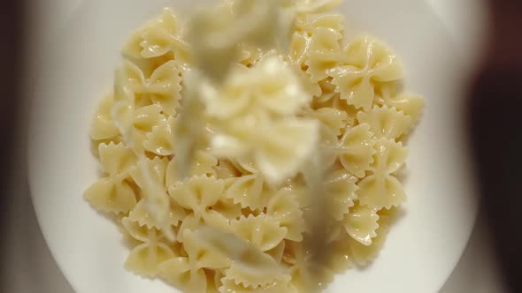 SLOW MOTION: Farfalle Pasta Falling Into A White Plate - Top View alt