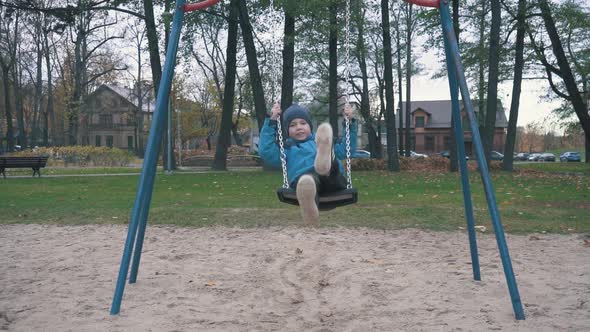 Boy is Swaying on Swing in Park at Autumn Day and Jumping Out in Slow Motion alt