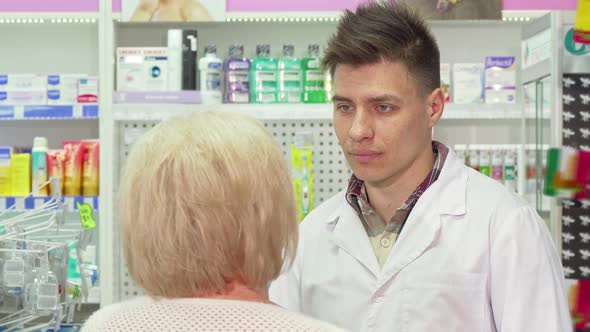 Young Male Pharmacist Talking To His Elderly Client alt