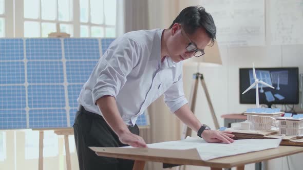 Asian Man Looking At The Blueprint With Model Small House With Solar Panel alt