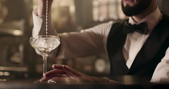 Close-up Shooting. Bartender Is Turning the Ice in Glass Using the Bar Spoon alt