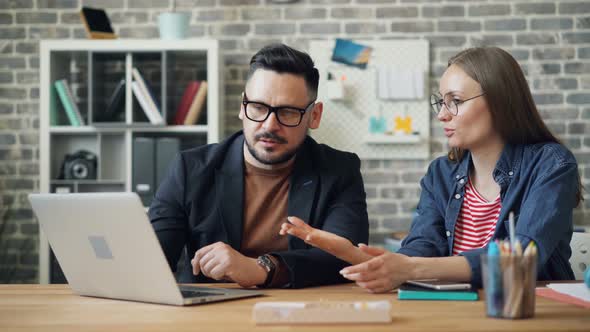 Man and Woman Looking at Laptop Screen and Talking During Workday in Office alt
