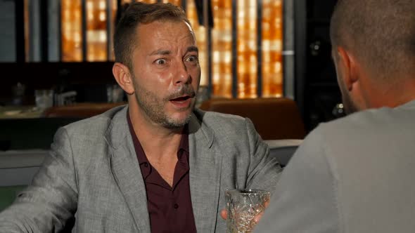 Mature Man Telling His Friend Something Expressively While Having Drinks alt