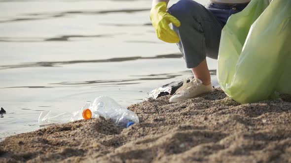 A Woman in Rubber Gloves Collects Various Garbage on the Shore of the Lake Closeup