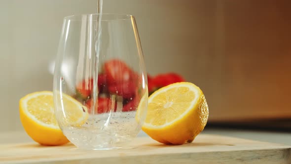 Empty Glass Between Two Part of Cut Lemon on Wooden Cutting Board alt