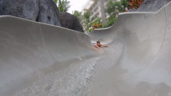 A boy plays on a waterslide water slide in a pool at a hotel resort. alt