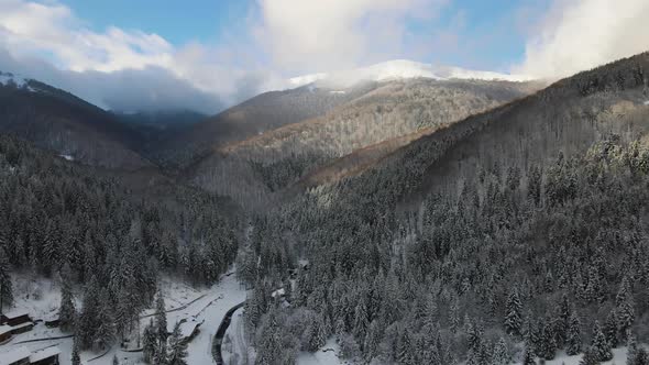 Aerial Winter Landscape with Small Rural Houses Between Snow Covered Forest in Cold Mountains alt