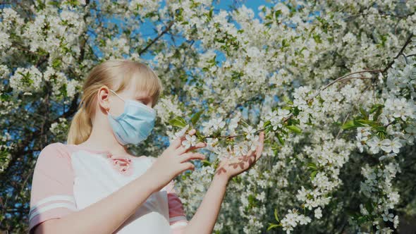 A Child Allergy Sufferer in a Mask Admires the Flowers on the Tree alt