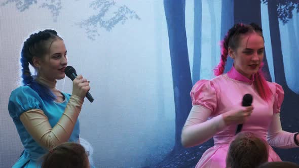 Two Young Woman Twins with a Microphone Lead Children Party on Stage. Animation alt