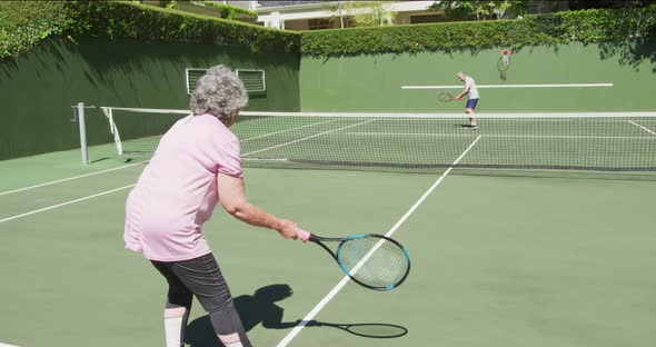 Caucasian senior couple paying a game of tennis on an outdoor court in the sun alt