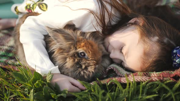 Little Girl and Brown Rabbit Lying on the Green Lawn and a Hug