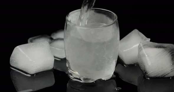 Pour Vodka Into Icy Glass with Ice Cubes Placed on a Black Background alt