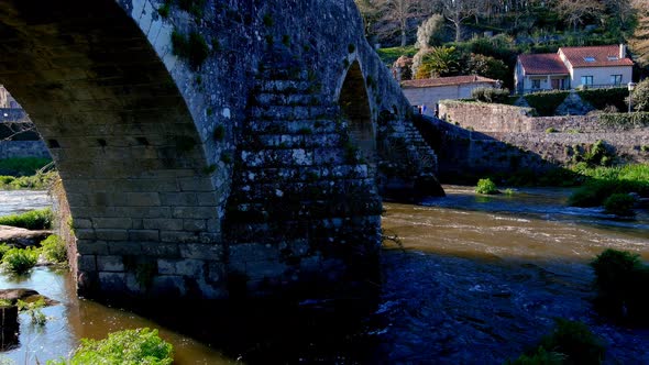 Aerial View Of Stone Arches Of Bridge of Ponte Maceira Over The River Tambre. Dolly Back alt
