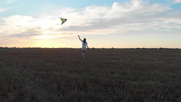 A Woman with a Kite Walks on a Beautiful Field at Sunset. Rest and Recreation in Nature