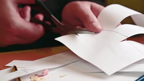 Man's hand holding up a sheet of baking paper and cut using a pair of scissors.