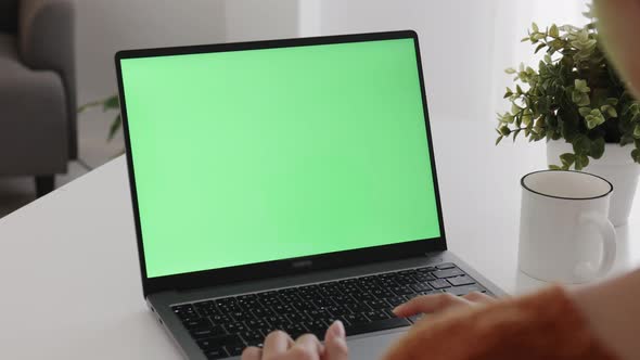 Young Asian woman using laptop computer at home with green blank monitor screen. alt