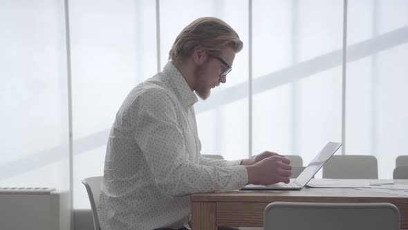 Successful Confident Bearded Businessman Working on a Laptop While Sitting at a Table alt