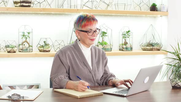 Modern Senior Business Lady Writing Company Profit in Her Notebook. alt