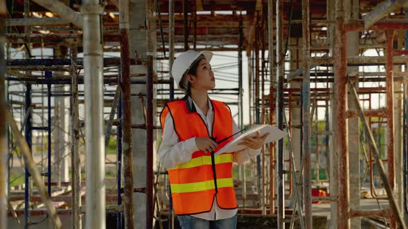 young Asian female engineer with blueprints is walking to check whether the construction work